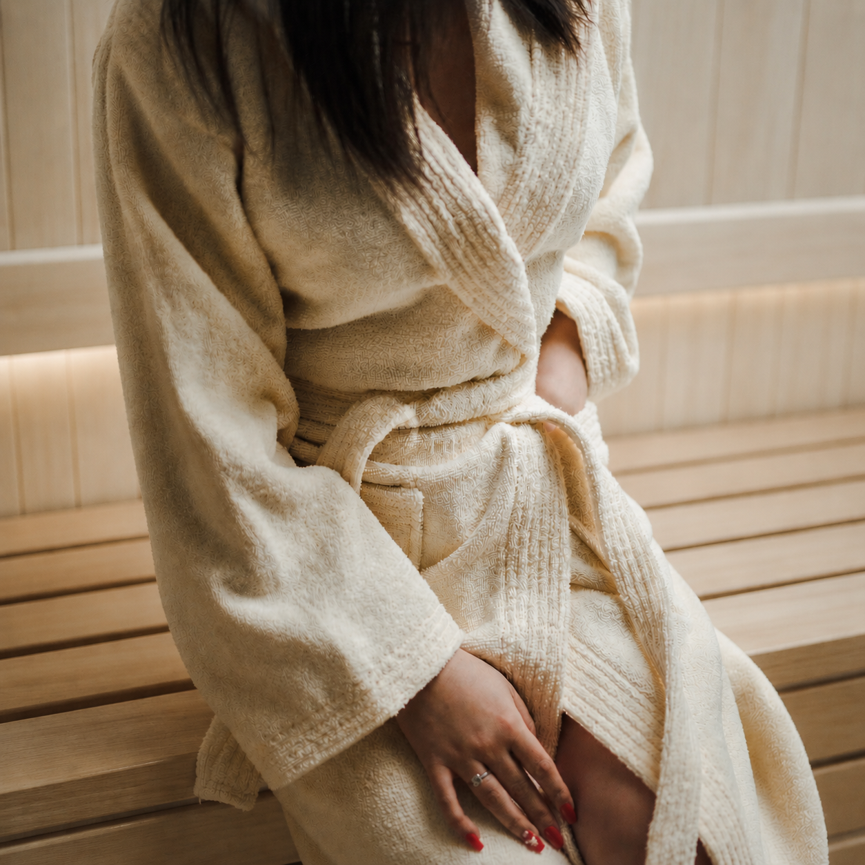 Vrouw zit in sauna met luxe crème badjas