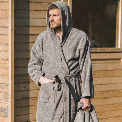 Man draagt een grijze badjas met capuchon buiten bij houten sauna